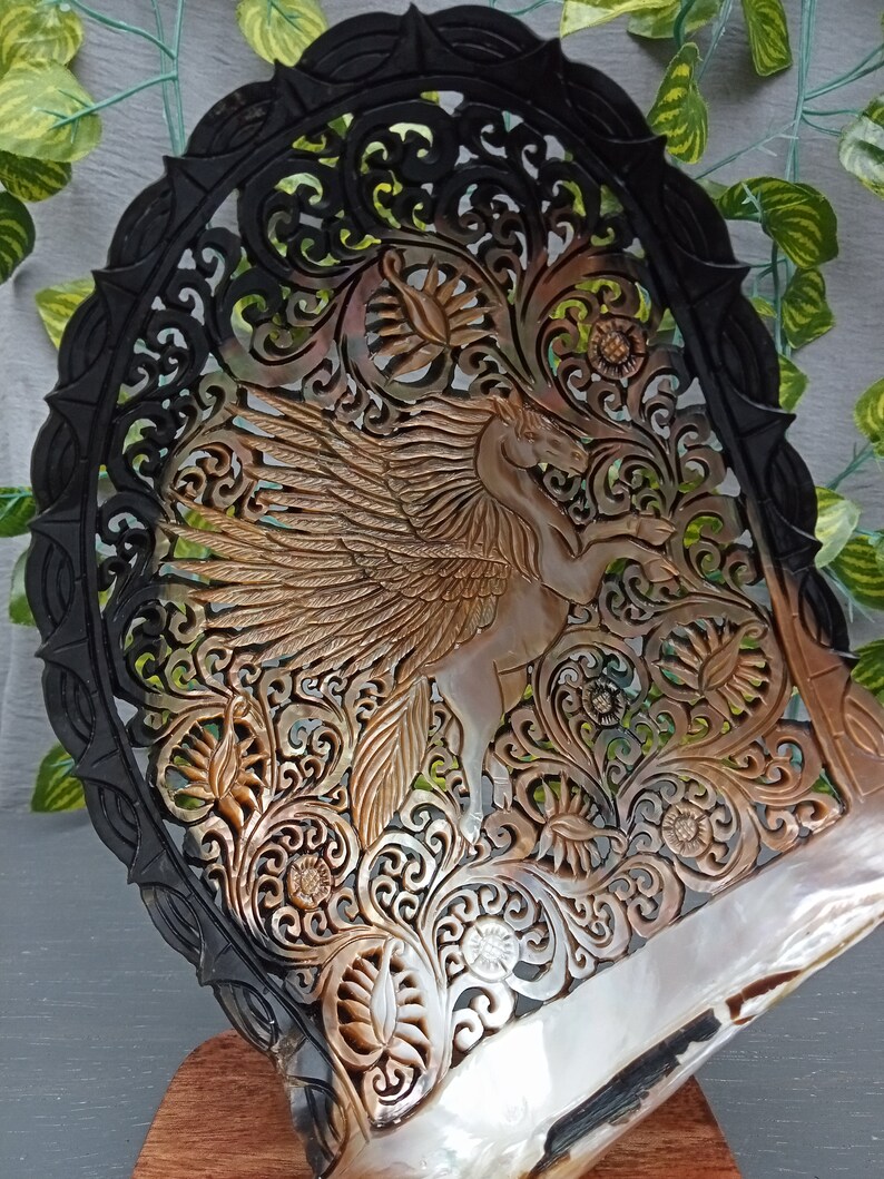 This is a real and natural mother of pearl shell polished and hand carved with wooden stand by a very skilled carving artist in his field. It is very detailed with pegasus design and has high artistic value