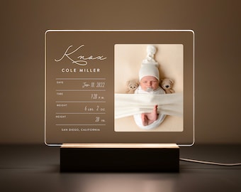 Puede incluir: Un marco de fotos de acrílico transparente con una base de madera blanca. El marco muestra una foto de un bebé recién nacido con un gorro blanco y dos ositos de peluche. El marco también incluye el nombre del bebé, Knox Cole Miller, la fecha de nacimiento, la hora, el peso (6 lb 2 oz), la altura (20 pulgadas) y la ubicación: San Diego, California.