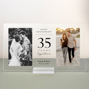 Op de afbeelding: Een transparant acryl fotolijstje met twee zwart-witfoto's en een witte kaart met de tekst "Happy Anniversary 35 Years Together Arman & Mina May 22, 1989".