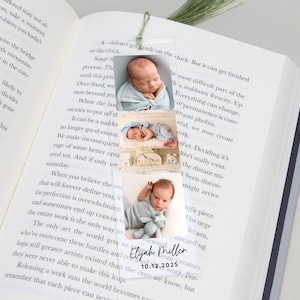 May include: A clear acrylic bookmark featuring three photos of a newborn baby. The bookmark includes the baby's name, "Elijah Miller," and the date "10.12.2025" in black text. The bookmark is placed on the pages of a book.