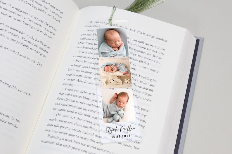 May include: A clear acrylic bookmark featuring three photos of a newborn baby. The bookmark includes the baby's name, "Elijah Miller," and the date "10.12.2025" in black text. The bookmark is placed on the pages of a book.