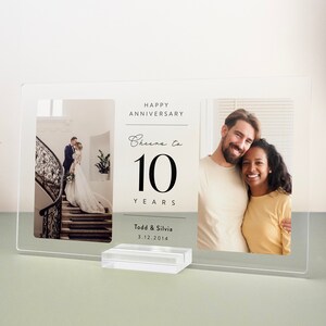 Op de afbeelding: Een helder acryl fotolijst met twee foto's. De linker foto toont een stel op een trap. De rechter foto toont een stel dat lacht. De tekst op het frame luidt "Happy Anniversary Cheers to 10 Years Todd & Silvia 3.12.2014".