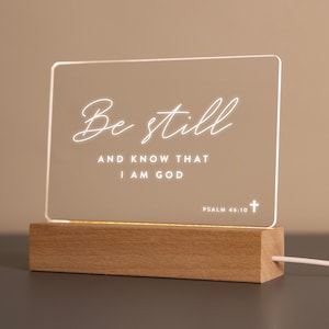 Personalized LED light featuring the comforting Bible verse "Be still and know that I am God" from Psalm 46:10, engraved on a clear acrylic plaque with a warm wooden base. Perfect for home décor, prayer spaces, or as an uplifting Christian gift.