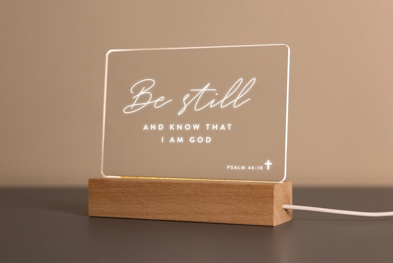 Personalized LED light featuring the comforting Bible verse "Be still and know that I am God" from Psalm 46:10, engraved on a clear acrylic plaque with a warm wooden base. Perfect for home décor, prayer spaces, or as an uplifting Christian gift.