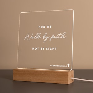 Personalized LED light featuring the inspiring Bible verse from 2 Corinthians 5:7: "For we walk by faith, not by sight." Engraved on a clear acrylic plaque with a warm wooden base, perfect for home décor, prayer spaces, or as a thoughtful Christian gift.