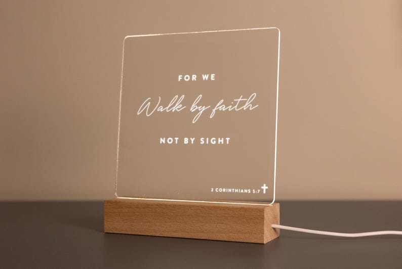 Personalized LED light featuring the inspiring Bible verse from 2 Corinthians 5:7: "For we walk by faith, not by sight." Engraved on a clear acrylic plaque with a warm wooden base, perfect for home décor, prayer spaces, or as a thoughtful Christian gift.