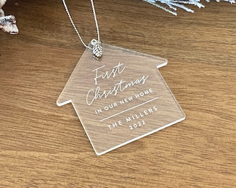 May include: Clear acrylic house-shaped Christmas ornament with the text "First Christmas in our new home The Millers 2022".