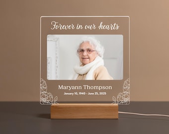 Könnte beinhalten: Ein Gedenklicht mit einem Foto einer älteren Frau, dem Text "Forever in our hearts" und dem Namen Maryann Thompson mit Daten. Das Licht steht auf einem Holzsockel und hat ein weißes Kabel.
