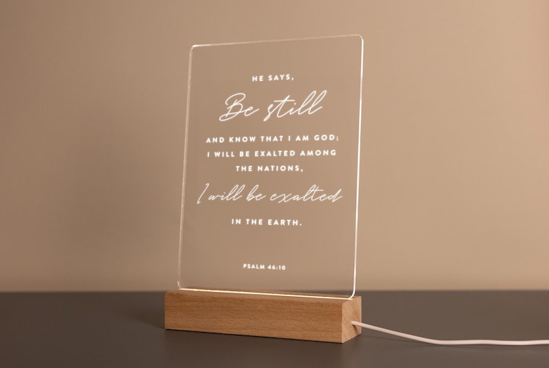 Personalized LED light featuring the calming Bible verse from Psalm 46:10: "He says, 'Be still and know that I am God; I will be exalted among the nations, I will be exalted in the earth.'" Engraved on a clear acrylic plaque with a warm wooden base, perfect for home décor, prayer spaces, or as a thoughtful Christian gift.