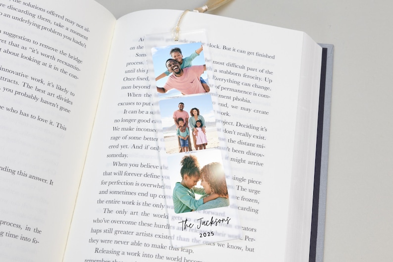 May include: A personalized bookmark featuring three family photos. The bookmark includes the text "The Jacksons" and the year "2025". It is hanging from a book.