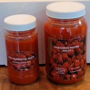 May include: Two glass jars of red habanero pepper paste. The smaller jar is labeled "Red Habanero Paste" with the company name "Zozoma Farms, Inc." and the ingredients "Fresh Ground Pepper" and "Pickling Salt". The larger jar is labeled "Habanero Pepper Paste" with the ingredients "Fresh Ground Peppers" and "Pickling Salt". The label also includes the company name "Zozoma Farms" and the location "Snellville, Georgia".