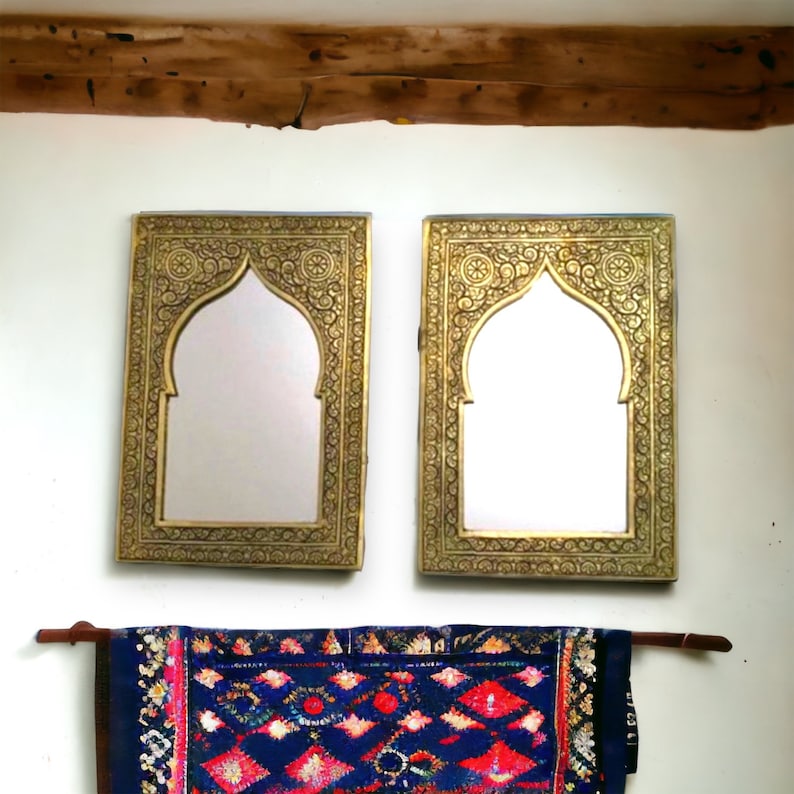 May include: Two ornate gold-coloured framed mirrors with arched tops and intricate designs. A blue and red patterned rug hangs below the mirrors.