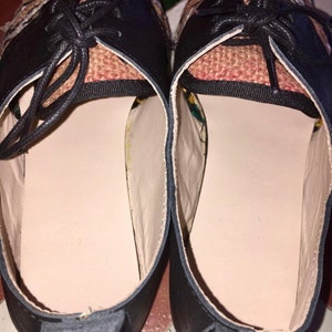 May include: Pair of black leather shoes with woven fabric detailing on the upper. The shoes have black laces and a light-colored interior. The soles are a neutral color, and the shoes appear to be new.