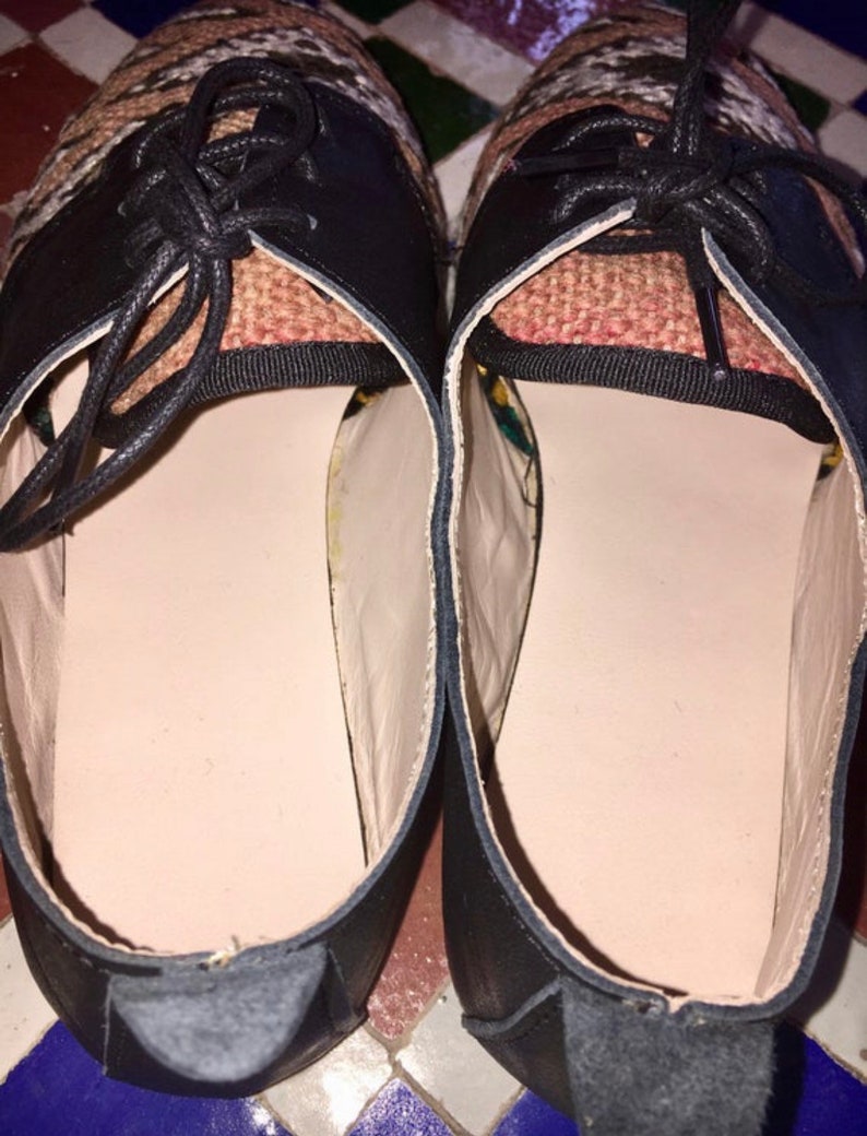 May include: Pair of black leather shoes with woven fabric detailing on the upper. The shoes have black laces and a light-colored interior. The soles are a neutral color, and the shoes appear to be new.