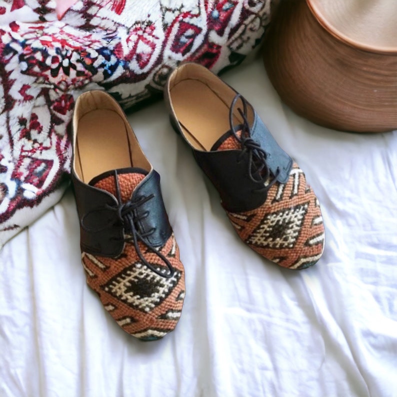 May include: A pair of brown and black oxford shoes with a woven geometric pattern on the toe and sides. The shoes have black leather detailing and laces. The shoes are displayed on a white surface.