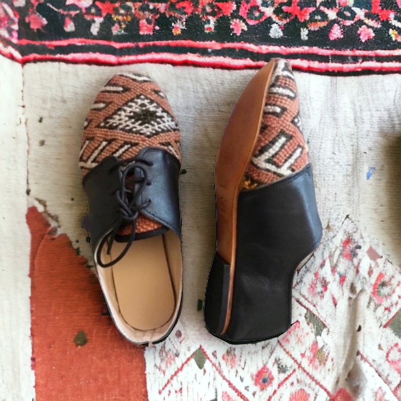 May include: Pair of handmade shoes with a unique design. The uppers feature a woven textile in shades of brown, tan, and white, while the toe and heel are black leather. The shoes have laces and a leather sole. A stylish and comfortable footwear option.