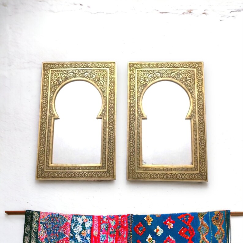 Puede incluir: Dos espejos ornamentados de color dorado con aberturas arqueadas. Los espejos est&aacute;n colocados contra una pared blanca.