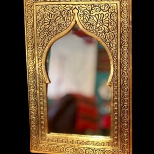 May include: An ornate gold-coloured mirror with a decorative frame featuring intricate floral patterns. The mirror has an arched top and a rectangular shape.