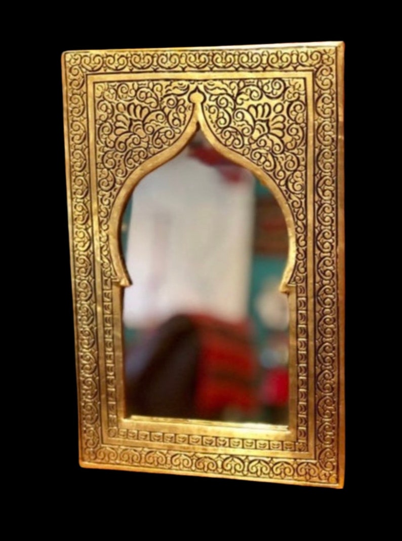 May include: An ornate gold-coloured mirror with a decorative frame featuring intricate floral patterns. The mirror has an arched top and a rectangular shape.
