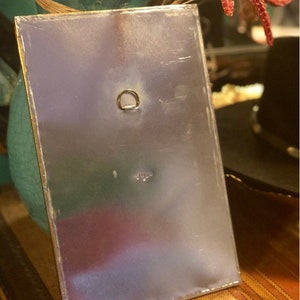 May include: A silver metal sign with a gold border and a small metal ring on the top. The sign is blank.
