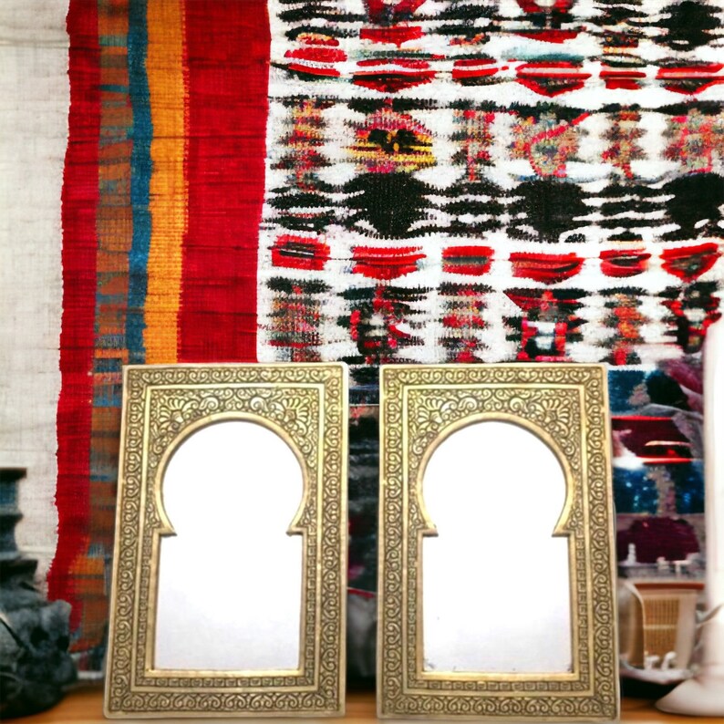 Puede incluir: Dos espejos con marcos ornamentados de color dorado con parte superior arqueada, colocados sobre una alfombra de patrones coloridos.