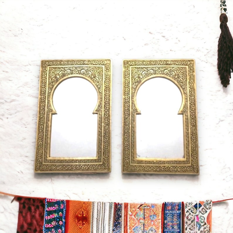 Puede incluir: Dos espejos ornamentados de color dorado con dise&ntilde;os intrincados y aberturas arqueadas. Los espejos est&aacute;n colgados en una pared blanca.