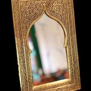 May include: An ornate gold-coloured mirror with a decorative frame featuring intricate floral patterns. The mirror has an arched top and a rectangular shape.