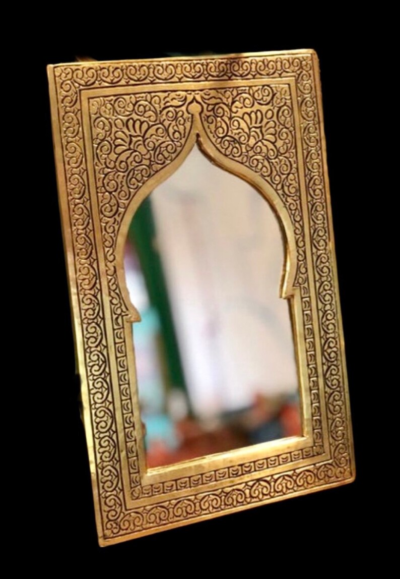 May include: An ornate gold-coloured mirror with a decorative frame featuring intricate floral patterns. The mirror has an arched top and a rectangular shape.