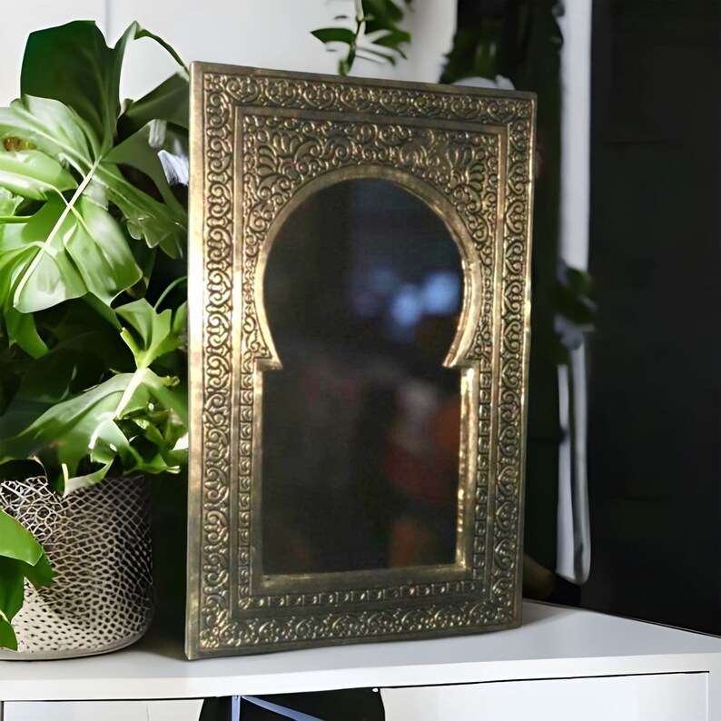 Puede incluir: Un espejo de metal dorado con un marco ornamentado y una abertura en forma de ojo de cerradura. El marco tiene intrincados dise&ntilde;os florales.
