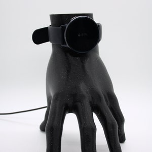Puede incluir: Un soporte de carga impreso en 3D con forma de mano negra con un reloj inteligente negro en la parte superior. La pantalla del reloj inteligente muestra un 61% de bater&iacute;a.
