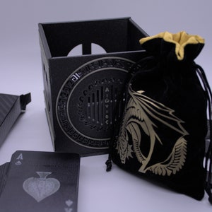 May include: A black playing card deck, a black box with a dragon design, a black velvet bag with a gold dragon design, and a black card holder with a dragon design.