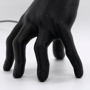 Puede incluir: Una escultura de mano negra con una superficie texturizada. La mano est&aacute; posada con los dedos extendidos y ligeramente curvados.