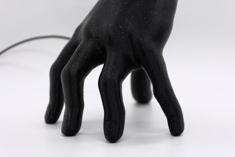 Puede incluir: Una escultura de mano negra con una superficie texturizada. La mano est&aacute; posada con los dedos extendidos y ligeramente curvados.