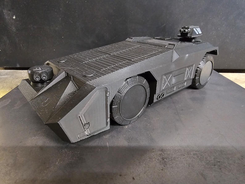 May include: A black, detailed, 3D printed model of a futuristic military vehicle with a raised platform and a turret on top.