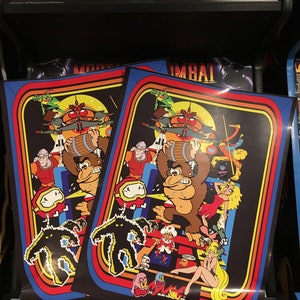 May include: Two colorful posters with a retro video game theme. The posters feature a large gorilla character, a barrel, and other characters. The posters have a rainbow stripe border and the text "Mortal Kombat" at the top.