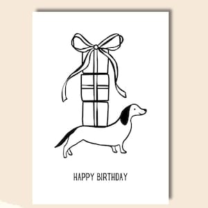 May include: A black and white illustration of a dachshund carrying a stack of wrapped presents with a bow on top. The text "HAPPY BIRTHDAY" is below the dog.