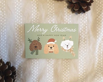 May include: A holiday greeting card with the text "Merry Christmas and a Happy New Year." The card features illustrations of three dogs wearing festive accessories. The card is light green and is surrounded by pine cones.
