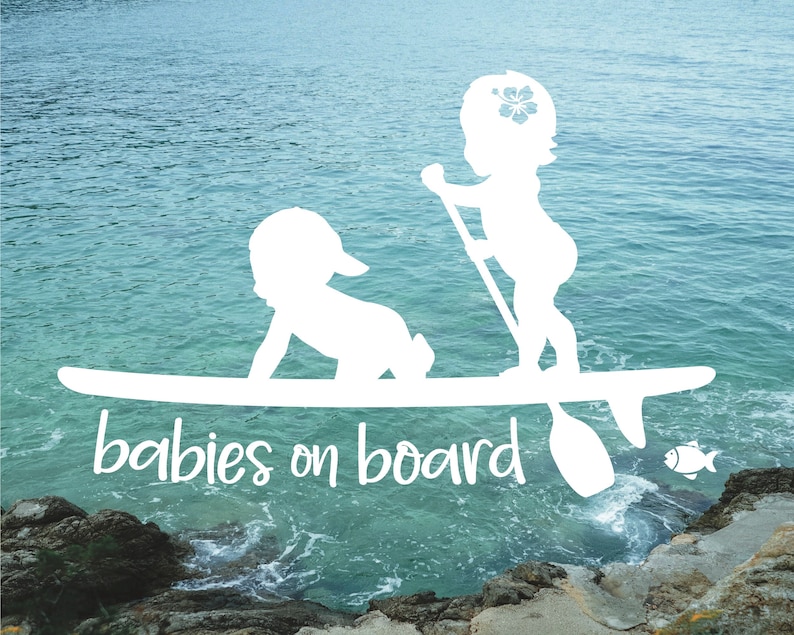May include: White silhouette of two babies on a surfboard with the text "babies on board" below. The surfboard is on top of blue water with a rocky shore in the background.