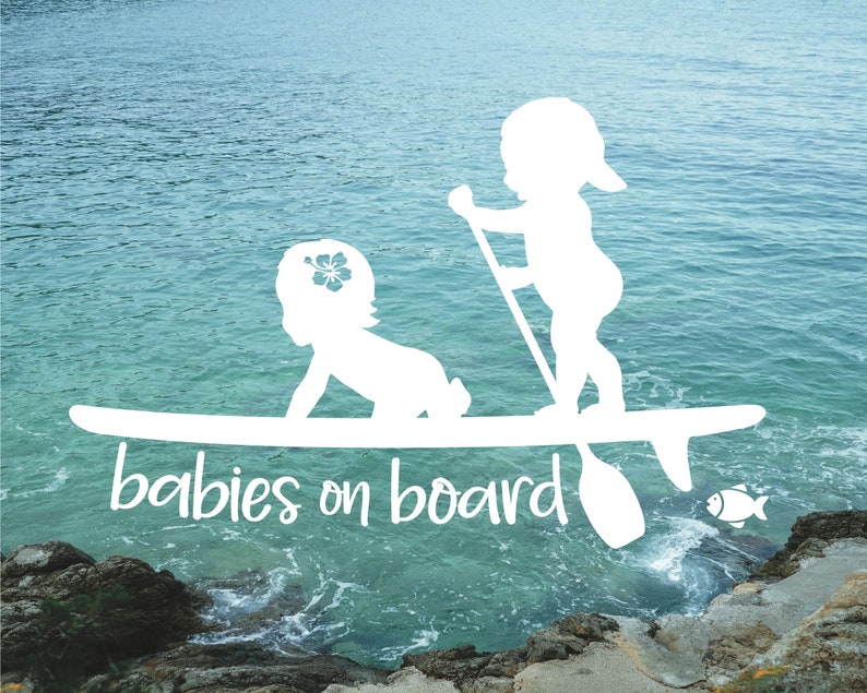 May include: White silhouette of two babies on a surfboard with the text "babies on board" in a cursive font. The background is a blue ocean with a rocky shore.