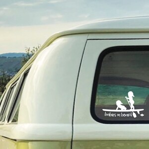 May include: White vinyl sticker with a silhouette of two children on a surfboard with the text "Babies on board".