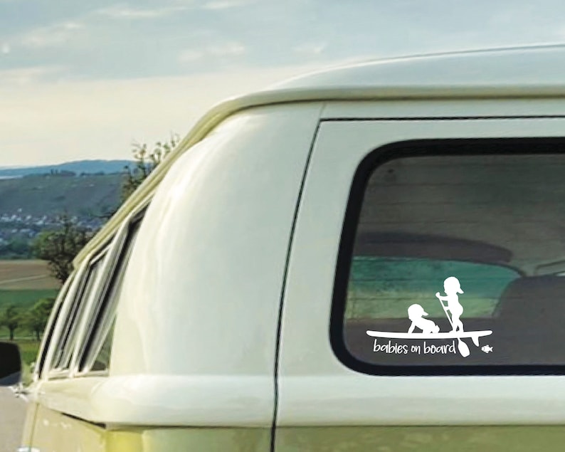 May include: White vinyl sticker with a silhouette of two children on a surfboard with the text "Babies on board".