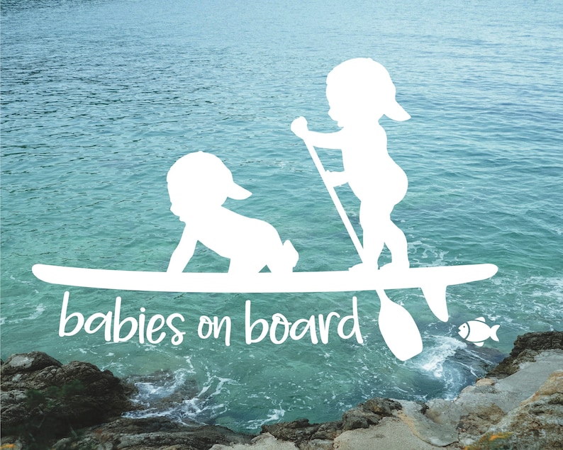 May include: White silhouette of two babies on a surfboard with the text "babies on board" in white. The background is a blue ocean with a rocky shore.