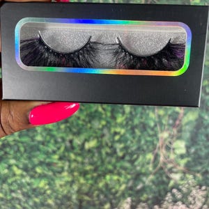 May include: A pair of black false eyelashes in a black and iridescent packaging. The eyelashes are long and full, with a wispy, layered design.