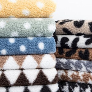 May include: A stack of soft, textured fabric rolls in various colors and patterns. The rolls include yellow with white polka dots, blue with white polka dots, and brown with white diamond shapes. Other rolls have animal print designs.