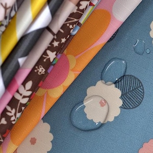 Könnte beinhalten: Nahaufnahme von Stoffmustern mit verschiedenen Designs. Die Stoffe zeigen florale, geometrische und abstrakte Muster in Farben wie Rosa, Gelb, Orange und Blau. Wassertropfen sind auf dem blauen Blumenstoff sichtbar.