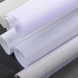 May include: Several rolls of white fabric are arranged diagonally. The rolls vary in texture, with some appearing smooth and others more textured. The fabric is tightly rolled, and the edges are visible.