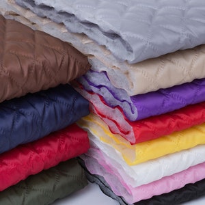 May include: A stack of quilted fabric in various colours, including brown, navy blue, red, green, yellow, white, pink, and purple. The fabric has a diamond pattern and is likely used for quilting or crafting projects.