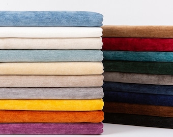 Op de afbeelding: Een stapel stofstalen in verschillende kleuren, waaronder blauw, wit, beige, grijs, geel, oranje, paars, rood, groen en bruin. De stof heeft een corduroy-textuur.