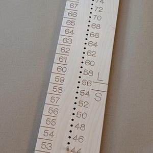 May include: A wooden measuring tool with a numbered scale from 50 to 74. The tool has two rows of small metal pins, one on each side of the scale. The scale is labelled "L" and "S" at the bottom.