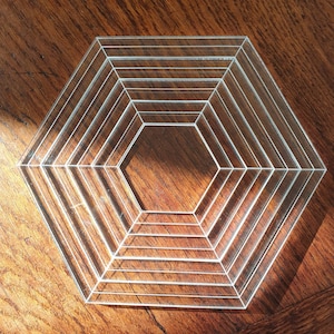 May include: A clear acrylic hexagon-shaped coaster with concentric rings. The coaster has a layered design with multiple rings.